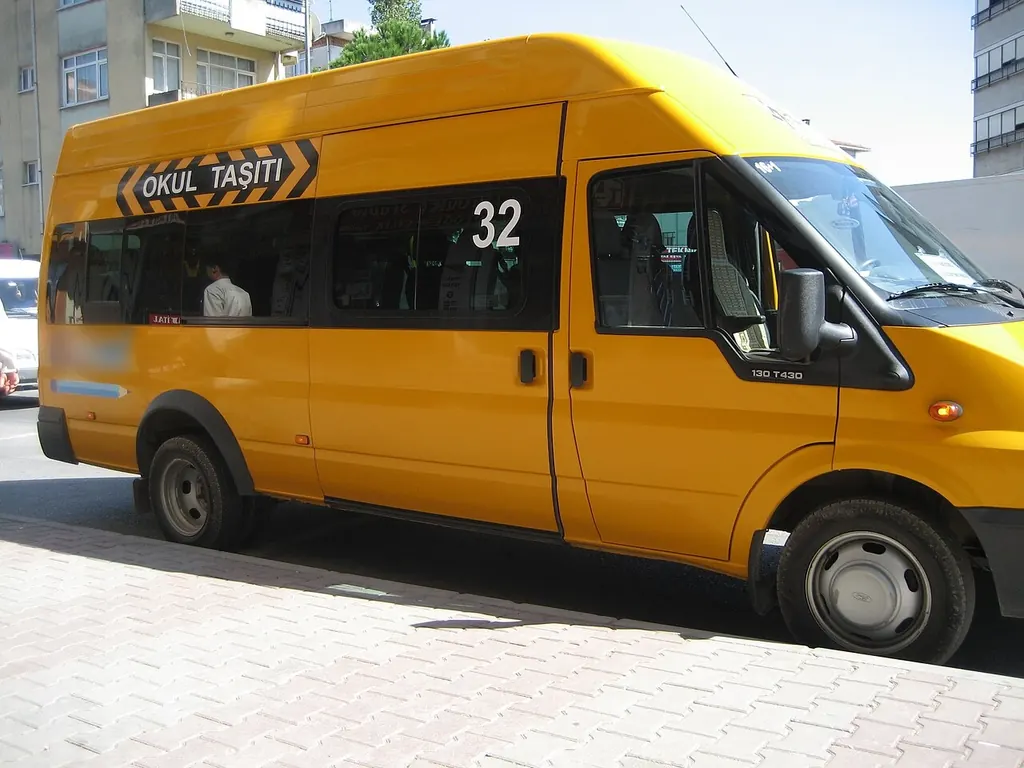 Üzerinde "OKUL TAŞITI" yazan sarı öğrenci servisi, kaldırım kenarında bekliyor.