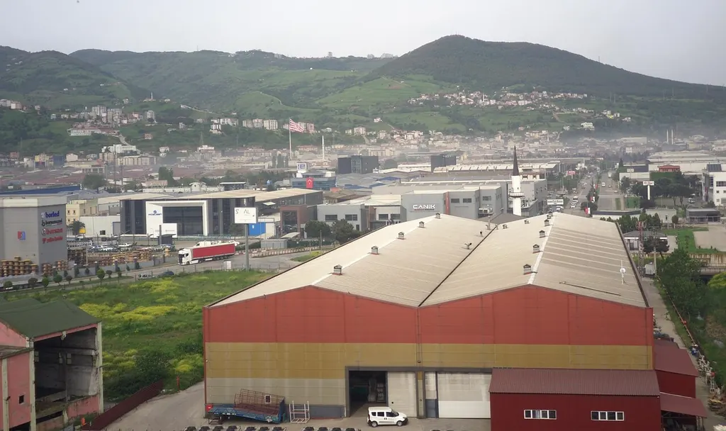 Samsun Organize Sanayi Bölgesi'nde fabrika binaları; arkada yeşil tepeler ve Türk bayrağı.