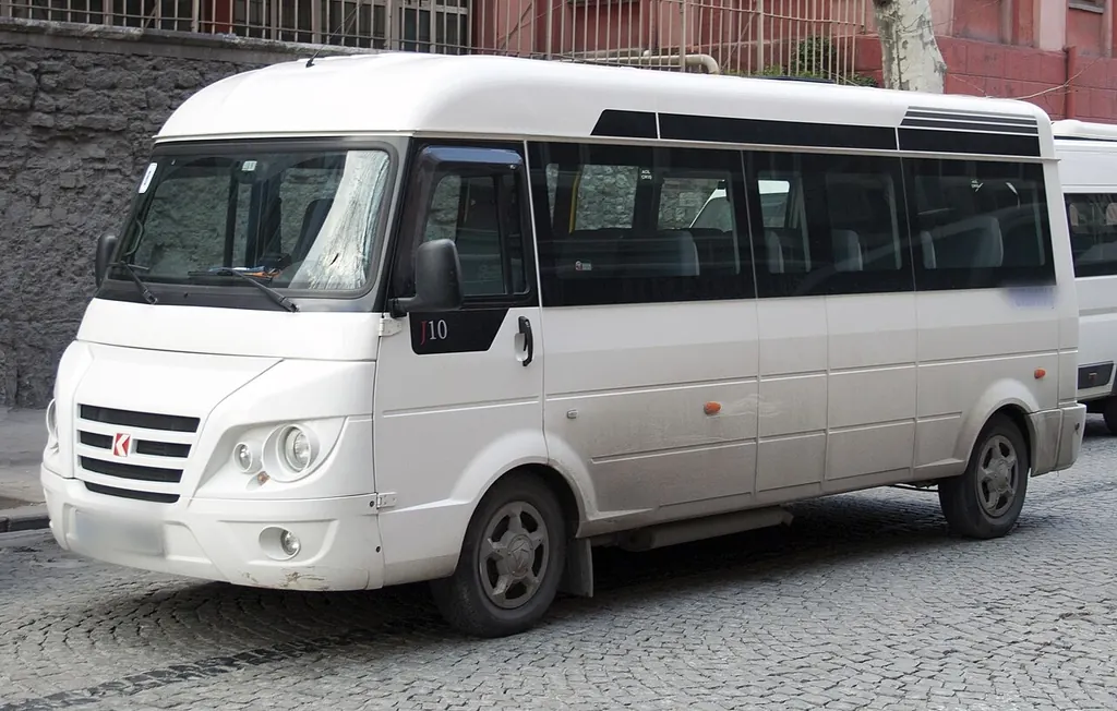 Arnavut kaldırımlı bir sokakta park etmiş beyaz servis midibüsü.